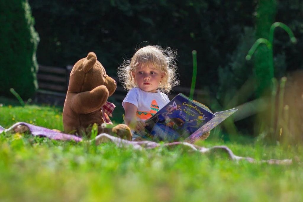 child reading book in garden with bear